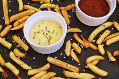  taze patates kızartması ve tuz taneleri ve baharatlar yalan koyu mermer arka plan, ketçap dolu bir kapta kızartılmış altın sarısı taze patates kızartması