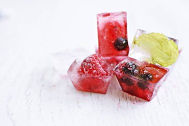 Yaz aylarında serinletici soğutma olarak, hafif ahşap bir yüzey üzerinde yalan içinde donan çeşitli çilek ile buz küpleri - Buz küpleri lezzetli ve organik çilek