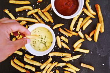  taze patates kızartması ve tuz taneleri ve baharatlar yalan koyu mermer arka plan, ketçap dolu bir kapta kızartılmış altın sarısı taze patates kızartması