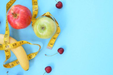 Elma, kiraz ve muz gibi farklı meyve türleri tek ayaklı bir taban üzerinde yatmaktadır ve bir ölçüm bandına sarılır - eğlenceli kılan sağlıklı kilo kaybı için kavram