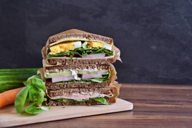 Sağlıklı bir diyet olarak peynir, sosis, yumurta ve salata ile ayçiçeği tohumu ekmek çeşitli sandviç koyu bir arka plan üzerinde yığılmış 