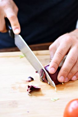 Bir kişi taze gevrek sağlıklı salata için ahşap bir tahta üzerinde kırmızı soğan keser - kişinin elinde yakın çekim - taze organik sebze ile sağlıklı beslenme için kavram