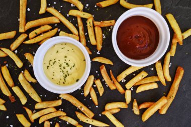  taze patates kızartması ve tuz taneleri ve baharatlar yalan koyu mermer arka plan, ketçap dolu bir kapta kızartılmış altın sarısı taze patates kızartması