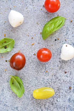 Taze domates ve lezzetli fesleğen ile arka plan - farklı çeşitli ve renk küçük domates fesleğen yaprakları ve küçük mozzarella topları ile birlikte, gri mermer yüzey üzerinde yalan 