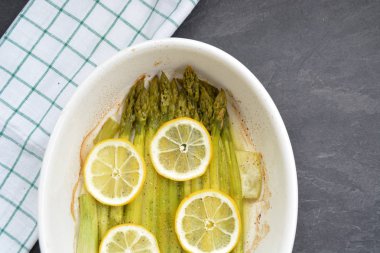 Limon dilimleri ile taze pişmiş yeşil kuşkonmaz ve baharat serpilir  