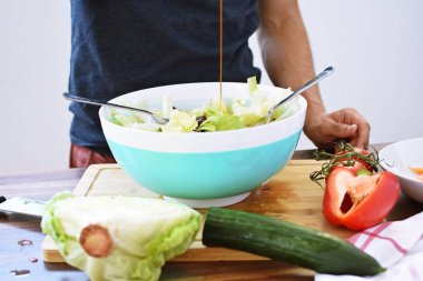 Taze yapılmış bir salata üzerine sos dökün - ahşap bir masada domates, salatalık ve biber ile taze salata bir kase yakın 