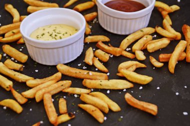  taze patates kızartması ve tuz taneleri ve baharatlar yalan koyu mermer arka plan, ketçap dolu bir kapta kızartılmış altın sarısı taze patates kızartması