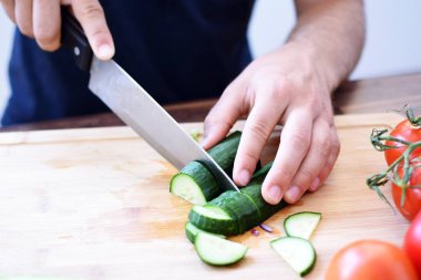 Bir kişi taze gevrek sağlıklı salata için ahşap bir tahta üzerinde bir salatalık kesiyor - kişinin elinde yakın çekim - taze organik sebze ile sağlıklı beslenme kavramı 