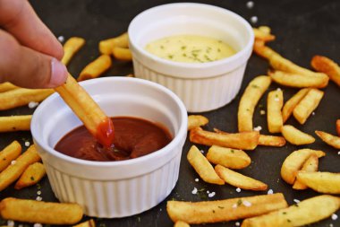 taze patates kızartması ve tuz taneleri ve baharatlar yalan koyu mermer arka plan, ketçap dolu bir kapta kızartılmış altın sarısı taze patates kızartması 