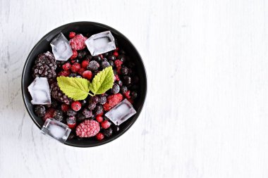 Parlak bir yüzeyde dondurulmuş yabani çilek dolu bir kase var, yanında metin veya diğer unsurlar için oda var - dondurulmuş yabani çilek ile kavram