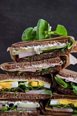 Sağlıklı bir diyet olarak peynir, sosis, yumurta ve salata ile ayçiçeği tohumu ekmek çeşitli sandviç ler koyu bir arka plan üzerinde yığılmış, fitness bir ima olarak bir ölçüm bandı yanında 