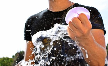 Bir adam açık havada duruyor ve elinde plastik bir su bombası tutar - su dolu bir balon tarafından yaz aylarında eğlenceli soğutma 