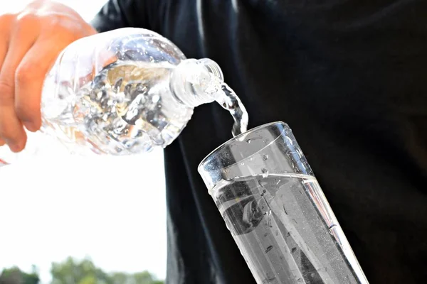 A man with a black shirt holds a plastic bottle with water in his hand, from which a momentum of water flies - concept for refreshing cooling with water in the summer