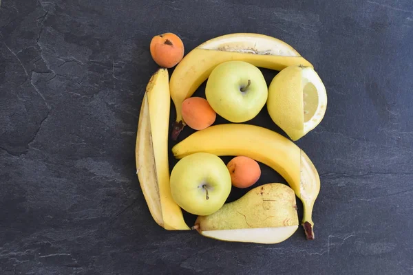 A bunch of yellow fruit like apples, pears and bananas lie on a flat surface, with a knife a square frame was cut into the fruit - perfectly arranged fruit as a frame