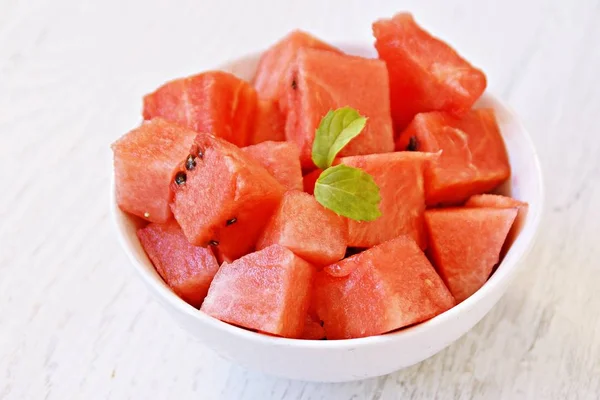 A bowl of watermelon cubes lye in a white bowl - fresh and sweet watermelon as a refreshment in summer on a white wooden surface