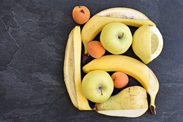 A bunch of yellow fruit like apples, pears and bananas lie on a flat surface, with a knife a square frame was cut into the fruit - perfectly arranged fruit as a frame