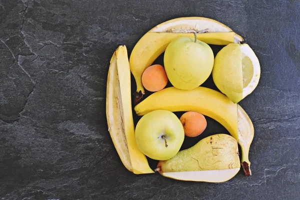A bunch of yellow fruit like apples, pears and bananas lie on a flat surface, with a knife a square frame was cut into the fruit - perfectly arranged fruit as a frame