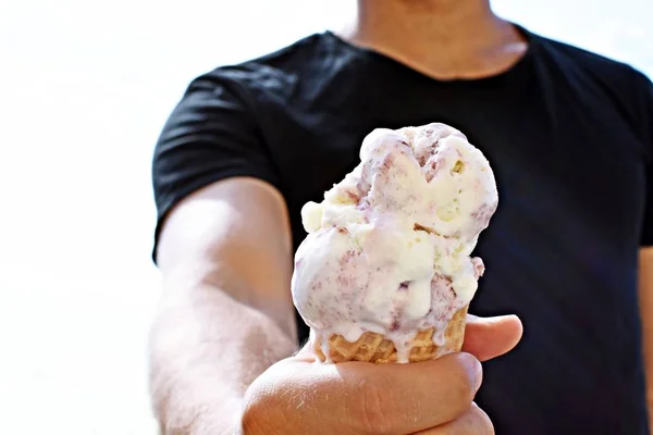 Closeup on the upper body of a man with shirt holding a waffle ice cream in hand. The ice cream balls Wildberry are already melting due to the heat - Too hot summer with refreshing cooling