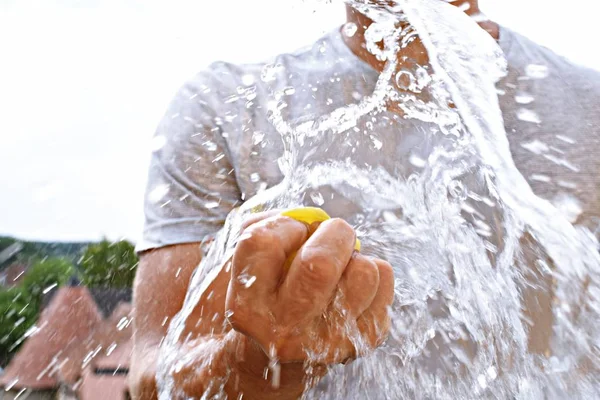 A man stands outdoors and holds a plastic water bomb in his hand - playful cooling in the summer by a balloon full of water