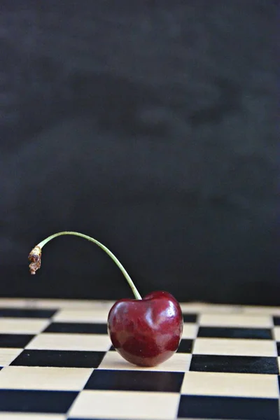 A single cherry lies on a gray marble surface