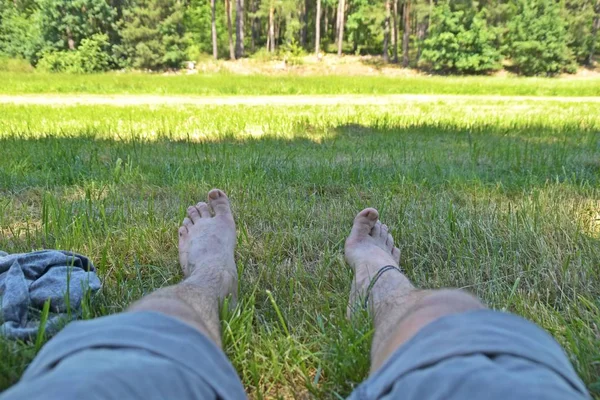 A young man lies on a green meadow beside a forest, the focus of the photo lies on his feet