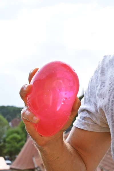 A man stands outdoors and holds a plastic water bomb in his hand - playful cooling in the summer by a balloon full of water