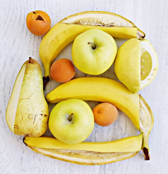 A bunch of yellow fruit like apples, pears and bananas lie on a flat surface, with a knife a square frame was cut into the fruit - perfectly arranged fruit as a frame