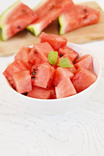 A bowl of watermelon cubes lye in a white bowl - fresh and sweet watermelon as a refreshment in summer on a white wooden surface