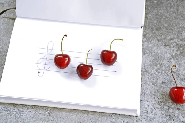 On a white block staves and a clef are drawn, cherries with stems serve as individual notes that lie on the sheet music - recipe with music notes and cherries