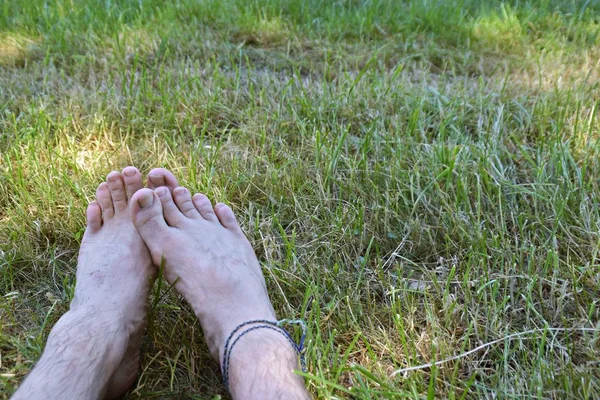 A young man lies on a green meadow beside a forest, the focus of the photo lies on his feet