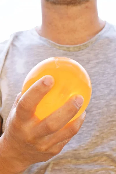 A man stands outdoors and holds a plastic water bomb in his hand - playful cooling in the summer by a balloon full of water