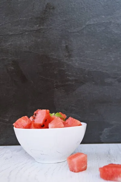 A bowl of watermelon cubes lye in a white bowl - fresh and sweet watermelon as a refreshment in summer on a white wooden surface