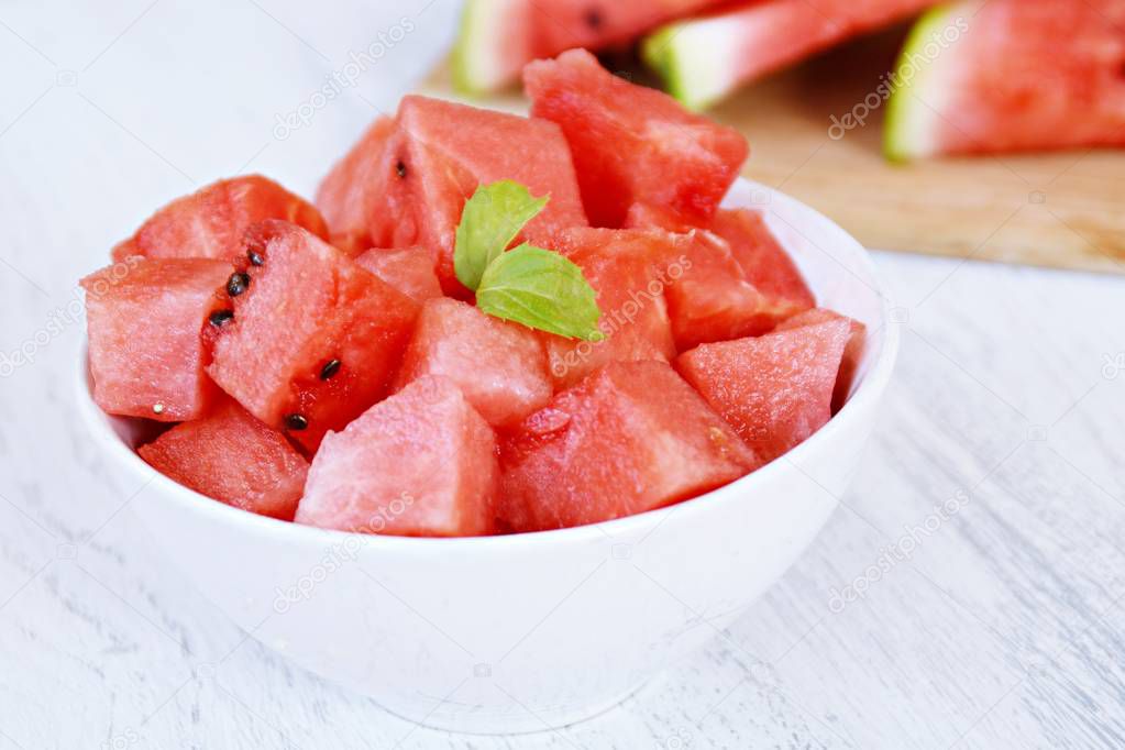 A bowl of watermelon cubes lye in a white bowl - fresh and sweet watermelon as a refreshment in summer on a white wooden surface