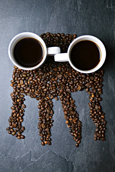 Coffee beans on a black background form the silhouette of a jellyfish and two cups of coffee form their eyes - concept with coffee and jellyfish