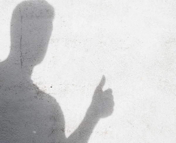 shadow of man gesturing thumb up on white wall