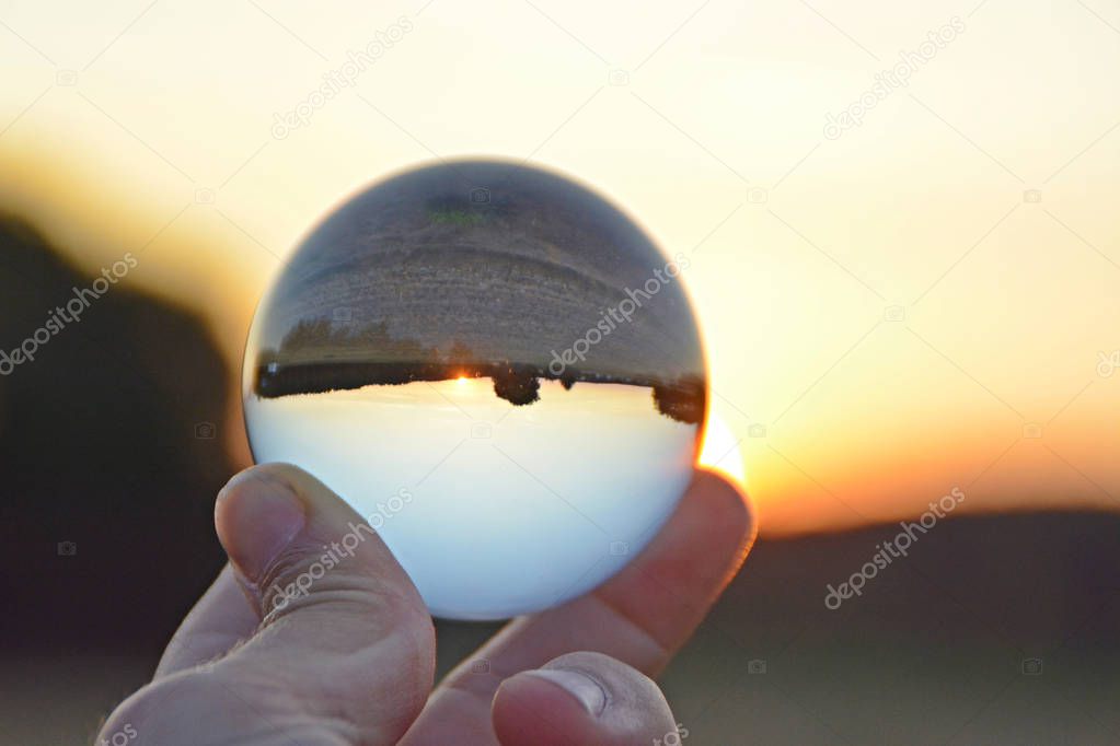 Holding a glass ball in his hand which shows a sunset in Germany