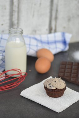 Homemade muffin with cream topping and chocolate, milk, eggs and flour on a kitchen surface