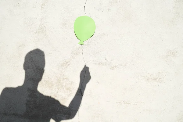 shadow of man holding balloon on white wall