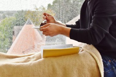 Pencere kenarında oturan adam lezzetli çikolatalı pastayla, arka plandaki yağmur damlalarıyla, bir kitap okuyor ve sonbaharda yağmurun ve sessizliğin tadını çıkarıyor.