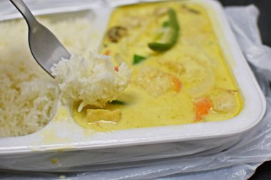 Çevreye zararlı plastik bir kutuda, yeşil körili yeşil köriye yakın plan yiyecek olarak, polistiren kutuda pirinçli Çin körisi ofisteki öğle yemeğini götürür.