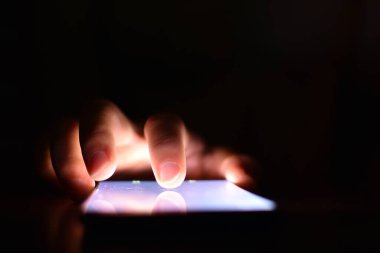 Karanlıkta aydınlatma ekranı olan akıllı telefon kullanan kişinin kısmi görüntüsü