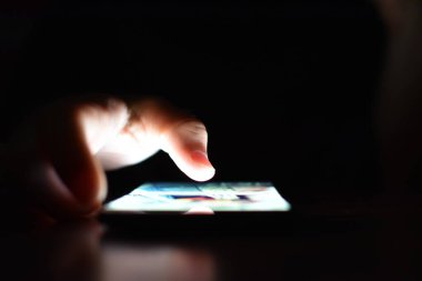 Karanlıkta aydınlatma ekranı olan akıllı telefon kullanan kişinin kısmi görüntüsü