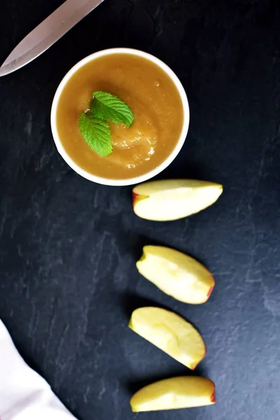 bowl of homemade apple puree with cinnamon and sugar in bowl surrounded by apple pieces on table