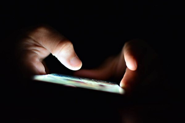 close-up partial view of person using smartphone with illuminated screen in darkness
