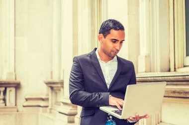 New York'ta okuyan, siyah ceket, beyaz gömlek giymiş, kampüste bina, aşağı bakıyor, dizüstü bilgisayar üzerinde çalışan eski office içinde oturan genç yakışıklı İspanyol Amerikan üniversite öğrencisi.