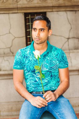 Genç Latin Amerikalı beyaz holding adam sen, yeşil desenli Polo gömlek giymiş sizi eksik gül, New York'taki eski sokakta oturan, uzağa arıyorsunuz, düşünme