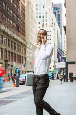 Cep telefonuyla konuşan sakallı genç Afrikalı-Amerikalı iş adamı New York'ta seyahat beyaz gömlek giymiş dizüstü bilgisayar taşıma, Manhattan Caddesi üzerinde yürüme. Arabalar, binalar zemin üzerine