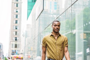 Genç Afro-Amerikan New York'ta seyahat pass cam duvar Midtown Manhattan'ın modern yüksek binalar ile sokakta yürürken yeşil kısa kollu gömlek giymiş yakışıklı.