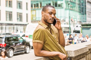 Sakallı, genç Afro-Amerikan Yeşil kısa kollu gömlek giymiş adam yarım duvara karşı duran, geri işlek cadde Midtown, Manhattan, New York'ta karşı karşıya, rahatlatıcı, cep telefonuyla konuşmak.