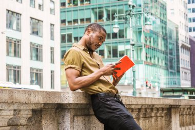 Kırmızı kitap okuma, sakallı, genç Afro-Amerikan Yeşil kısa kollu gömlek, siyah pantolon, Manhattan, New York'ta ofis dışında yarım duvar çit karşı ayakta adam arıyorum.